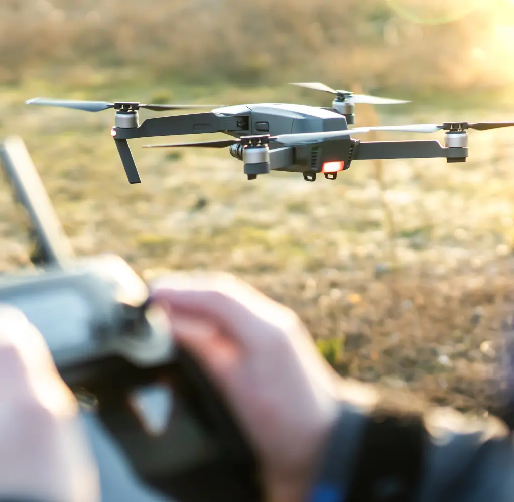 野外でドローンを操作する手元と飛行中のドローンを捉えた写真。